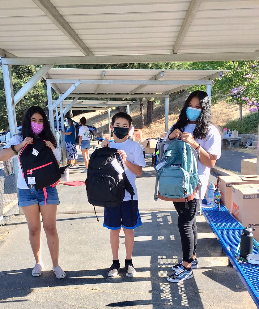 Three children standing under a shelter with backpacks