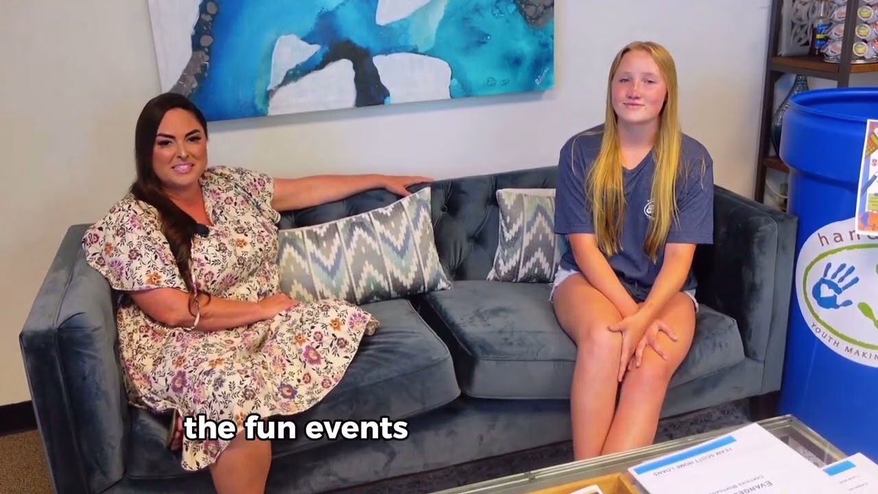 Two women sitting on a couch in front of a blue painting