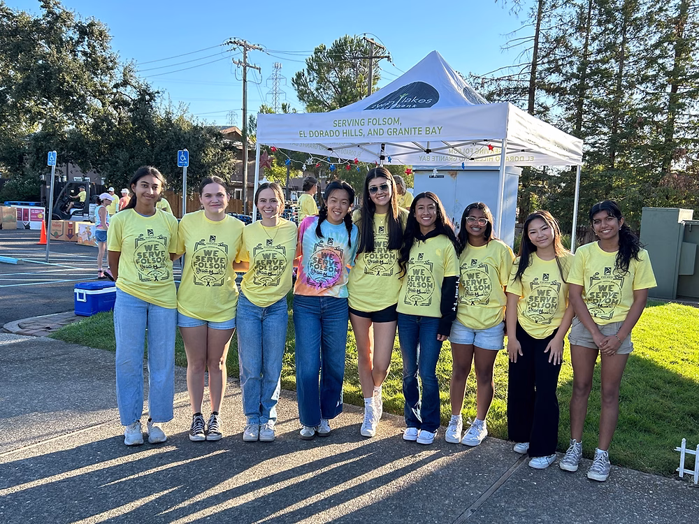 A group of young women in yellow shirts standing in front of a white pop-up tent with a logo and text on it.