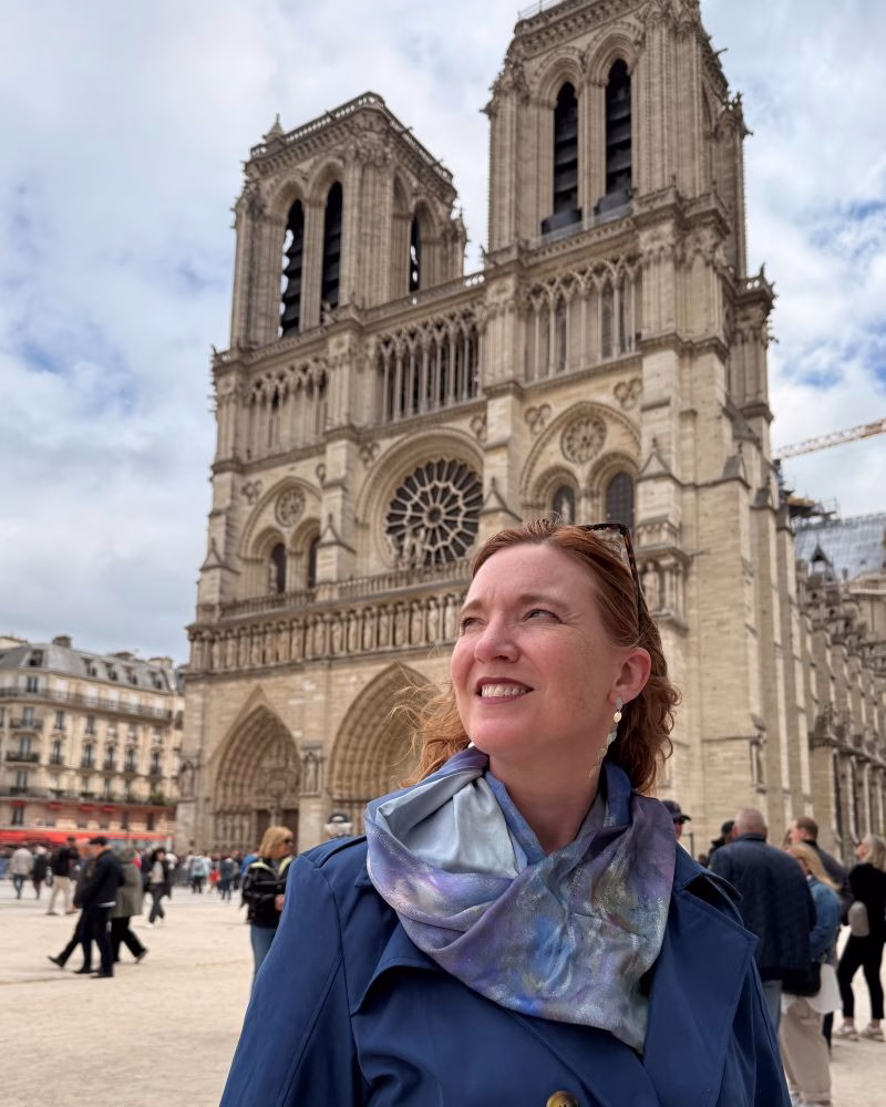 A woman stands in front of the iconic Notre Dame Cathedral in Paris, France, showcasing its grandeur and historical significance.