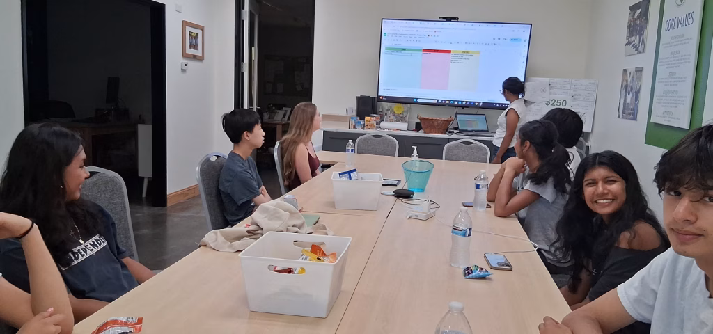 A group of young people sitting around a table watching a presentation on a large screen.