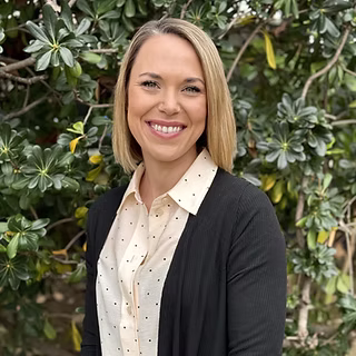 A woman standing in front of a tree, smiling at the camera.